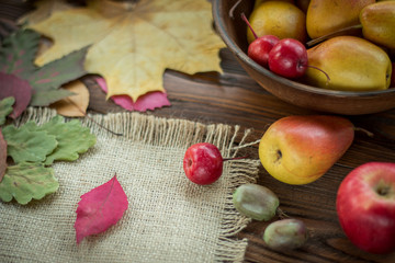 pears and red apples in clay plate, scattered with fallen leaves on wooden table - 167876402