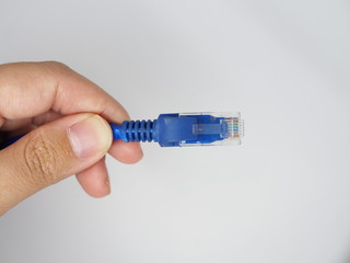 Left hand holding blue RJ45 LAN connector and cable, white background