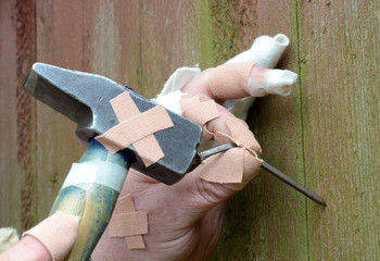 Ten thumbs, heavily "injured" homeworker tries to hammer a bent nail in a wall.