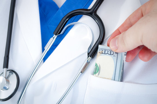 Corruption In The Medical System And High Cost Of Medical Bills Concept With A Doctor Wearing A White Lab Coat And A Stethoscope Has A Bill Slipped In By A Patient As A Bribe