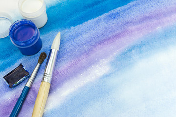 paintbrushes and paints on abstract blue watercolor textured background