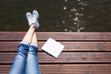 Woman relaxing by a lake with a book. Reading and summer holiday concept. 
