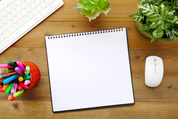 Blank notebook paper, keyboard, mouse and pens on wood table background
