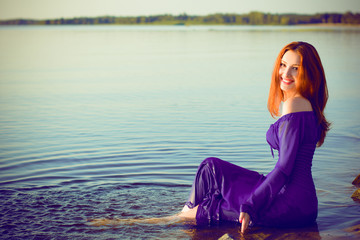 Gorgeous sexy young lady at evening sunlights around rocks and water. Woman wearing in purple long dress. Portrait in vintage style. Sweet woman rest on the sea