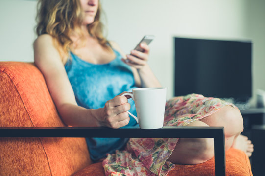 Young woman with cup and smart phone at home