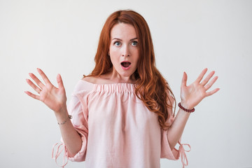 Portrait young woman with long curly red hair looking excited holding her mouth opened isolated on white wall.