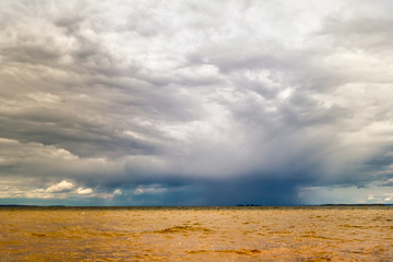 Thundercloud over the yellow river.
Horizontal frame. A dark blue cloud sheds rain in the yellow turbulent water