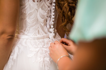 Fototapeta na wymiar Gorgeous, blonde bride in white luxury dress is getting ready for wedding. Morning preparations. Woman putting on dress.