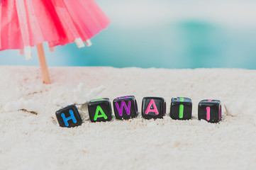 Word Hawaii is made of multicolored letters on snow-white sand against the blue sea. Tourism, rest, resort, sea, sun, beach