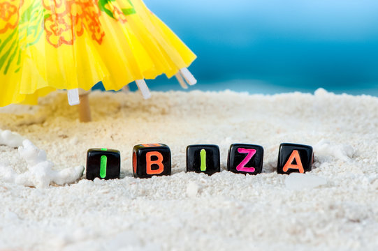 Word Ibiza is made of multicolored letters on snow-white sand against the blue sea. Tourism, rest, resort, sea, sun, beach
