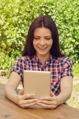 Young beautiful woman in casual shirt smiling while working with tablet. Portrait. Summer green park.