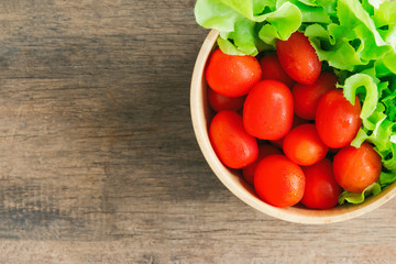 Fresh tomato and lettuce in wood bowl put on wood table. Top view or flat lay of tomato and green oak lettuce with copy space for background. Fresh green oak lettuce and tomato prepare for cooking.