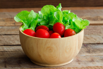 Fresh tomato and lettuce in wood bowl put on wood table. Side view close up of tomato and green oak lettuce with copy space for background. Fresh green oak lettuce and tomato prepare for cooking.