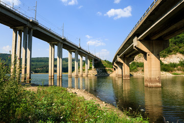 Railroad and automobile trestle bridges over Tsonevo dam, at Luda Kamchia river in Bulgaria against blue sky with clouds. Transport infrastructure details