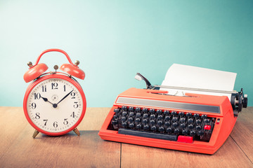 Retro typewriter, old alarm clock on table front mint green background. Vintage style filtered photo