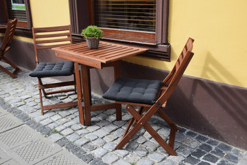 Wooden chairs and tables set on the sidewalk in front of the cafe