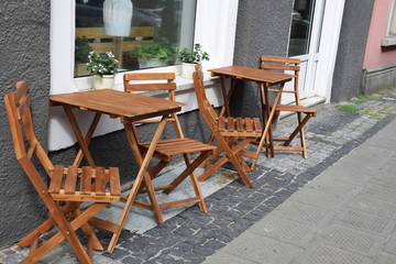 Wooden chairs and tables set on the sidewalk in front of the cafe