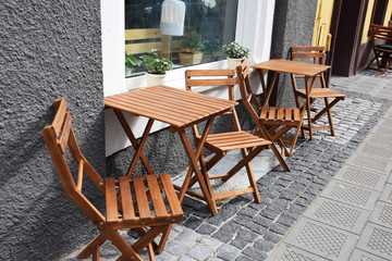 Wooden chairs and tables set on the sidewalk in front of the cafe