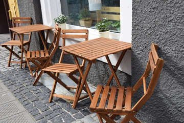 Wooden chairs and tables set on the sidewalk in front of the cafe