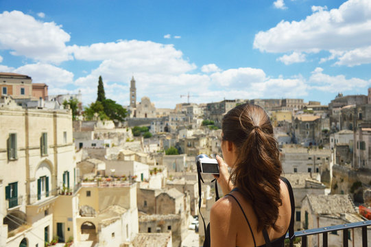 Young woman take photo with mirrorless camera to the old town of Matera. Beautiful traveller girl visit Sassi di Matera. Typical italian landscape. Female in south italian scenary