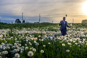 Young and attractive man in a suit standing in dandelion's field.