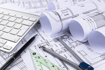 Architectural drawings of the modern house with computer keyboard. Architectural blueprints and blueprint rolls and a drawing instruments on the worktable. Drawing compass, plans.