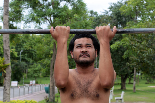 Asian man doing pull-ups on a horizontal bar in the park for healthy.