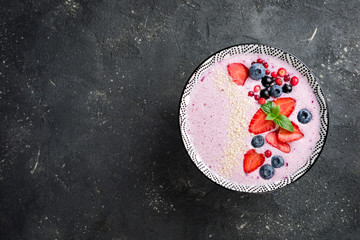 Smoothie bowl with berries, strawberries, blueberries, cranberries, currants. Pink smoothie on dark background. Healthy food and dieting concept. Top view, copy space