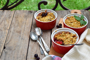 Fruits casserole or crumble with apples and berries in brown cup ramekin on wooden background. Copy space. Photographing with natural light
