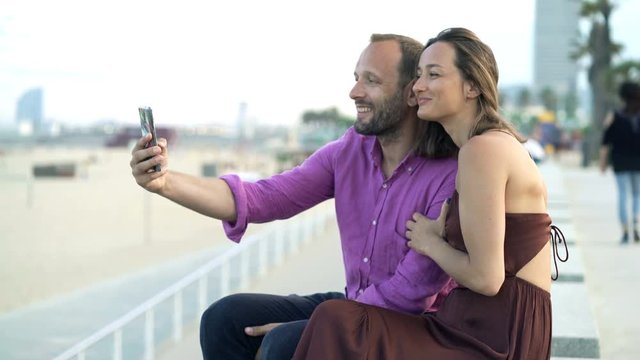 Young couple taking selfie photo with cellphone near beach in city 
