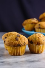 Three miniature vanilla muffins on marble surface in front of blue plate with some more muffins