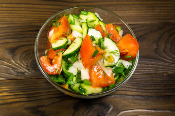 Fresh salad with tomato, cucumber, onion, parsley and dill in glass bowl on wooden table