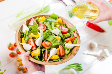 man pouring olive oil into healthy salad on kitchen