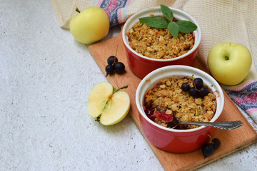 Fruits casserole or crumble with apples and berries in brown cup ramekin on light background. Copy...