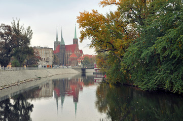 Gothic Church of St. John the Baptist in Wroclaw reflected in the Orda river on the background of the autumn park.