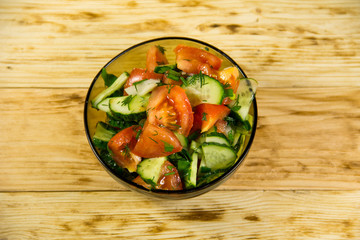 Fresh salad with tomato, cucumber, onion, parsley and dill in glass bowl on wooden table