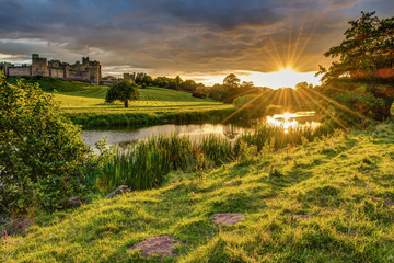 Fototapeta premium Promienie słoneczne nad rzeką Aln w Alnwick / The River Aln biegną przez Northumberland od Alnham do Alnmouth. Widzisz tutaj poniżej Alnwick Town i Castle na panoramie, gdy zachodzi słońce