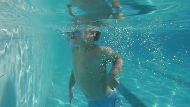 Boy diving in swimming pool. Super Slow Motion. Perfect for videos about: swimming, pools, summer fun, vacation, getaways, underwater footage, kids, beating the heat, and exercise.