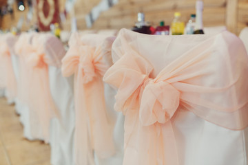 White chairs decorated with peach silk bows