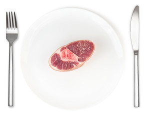 Raw pork knuckle on plate with fork and knife isolated