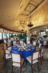 Round dinner table covered with blue cloth and decorated with green leaves