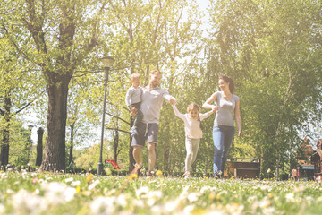 Naklejka na ściany i meble Happy parents playing with their children in the meadow. Family having fun in the spring day.