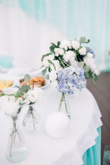 Little vases with blue and white flowers stand on the white table