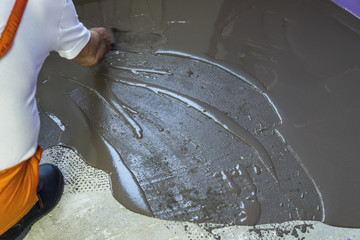 Worker puts a self leveling screed with trowel on cement floor i