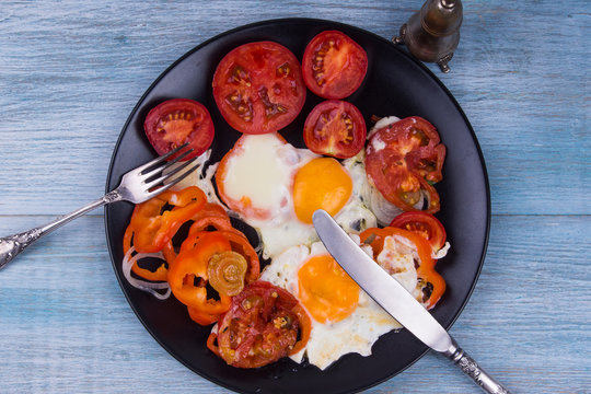 Fried eggs with fried peppers and tomatoes on a wooden background
