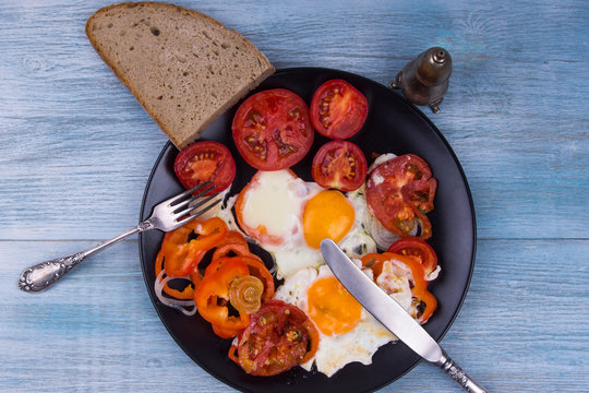 Fried eggs with fried peppers and tomatoes on a wooden background
