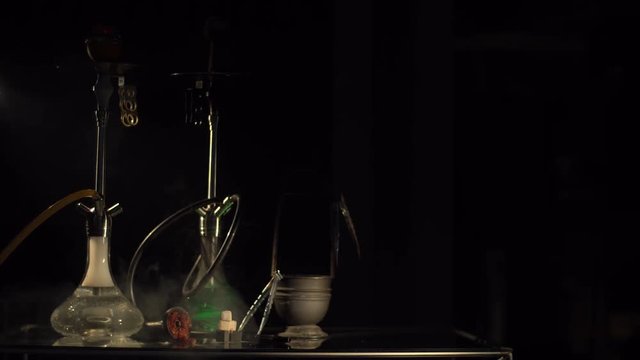 Horizontal view of the hookah composition of the smoke equipment. The thick cloud of smoke is covering the composition in the dark studio.