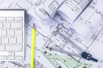 Architectural blueprint drawings of the modern house with computer keyboard. Architectural blueprints and blueprint rolls and a drawing instruments on the worktable. Drawing compass, plans.