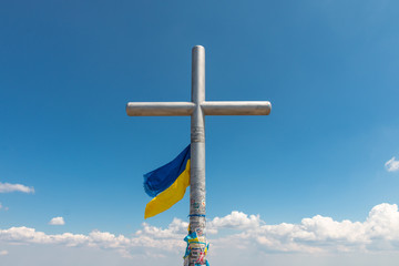 At the top of the mountain Hoverla (Goverla), the highest mountain of Ukraine, cross covered with Ukrainian flag, summer climbing, picturesque summer sky, Carpathians, Ukraine