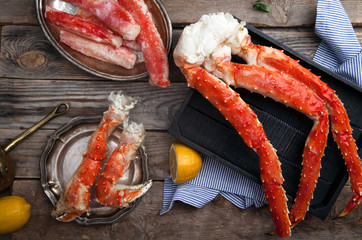 Fresh crab claws on black wooden tray on vintage wooden background with vintage plates and lemon slices. Horizontal composition
